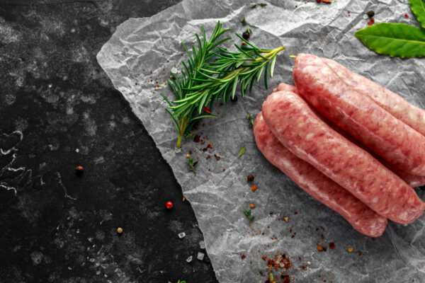 Freshly made raw breed butchers sausages in skins with herbs on crumpled paper