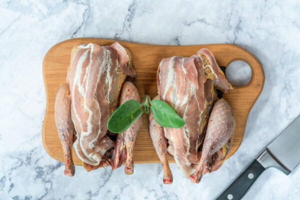 Two fresh raw pheasants wrapped in bacon prepared for cooking on wooden board - overhead view