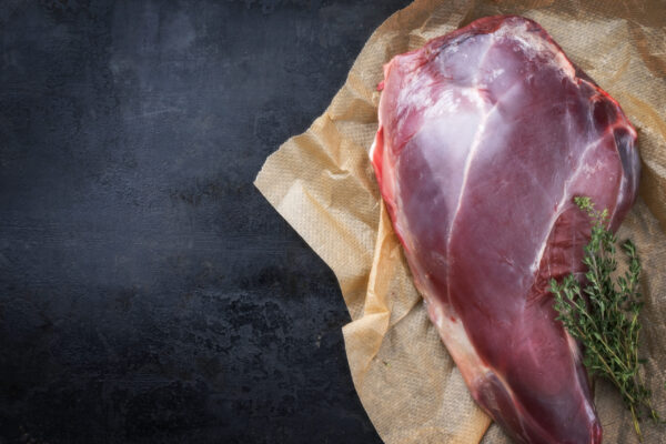 Raw aged leg of venison with bone and thyme as top view on brown paper with copy space left